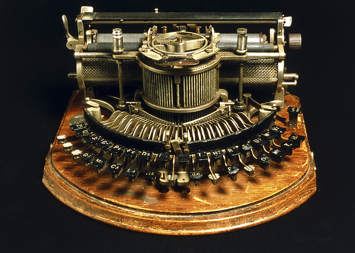 View of an early typewriter Early typewriter. View of an early typewriter. Machines like this one appeared in the late 19th century. Paper was held between the two rubber rollers  top . The letter keys  lower centre  are arrayed in a semi circular fashion. This was typical of early typewriters. When a key was struck the mechanism would cause the corresponding typebar to strike an inked ribbon. The inked ribbon was held on a spool at upper centre. The striking of the ribbon would cause an ink impression on the paper underneath. Once a character was printed, the paper would be automatically moved on one character space.