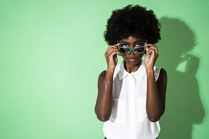 Studio portrait Young woman wearing sunglasses while standing green background
