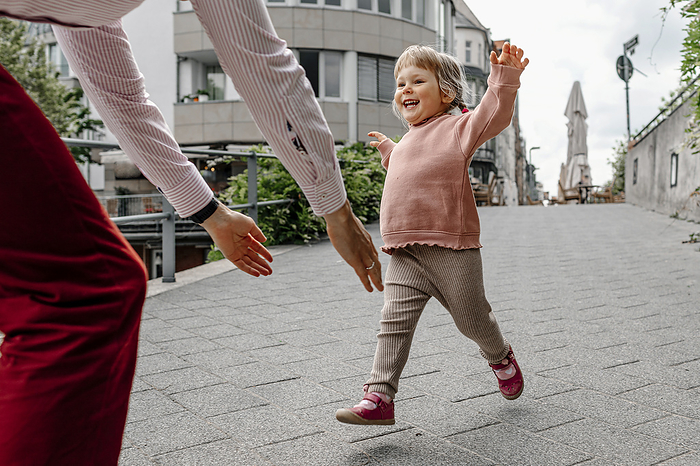 young family on a walk, D sseldorf, Germany Cheerful daughter running towards her father while playing on street in city