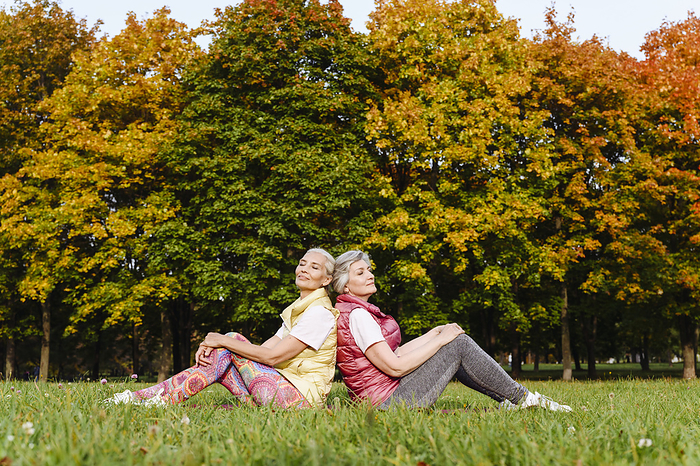 Moscow, Russia. Two mature women wearing sport clothes relaxing outside Mature female friends with eyes closed leaning on each others back at autumn park