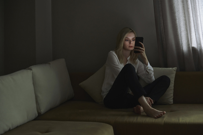 Blond woman using smart phone while sitting on sofa at home