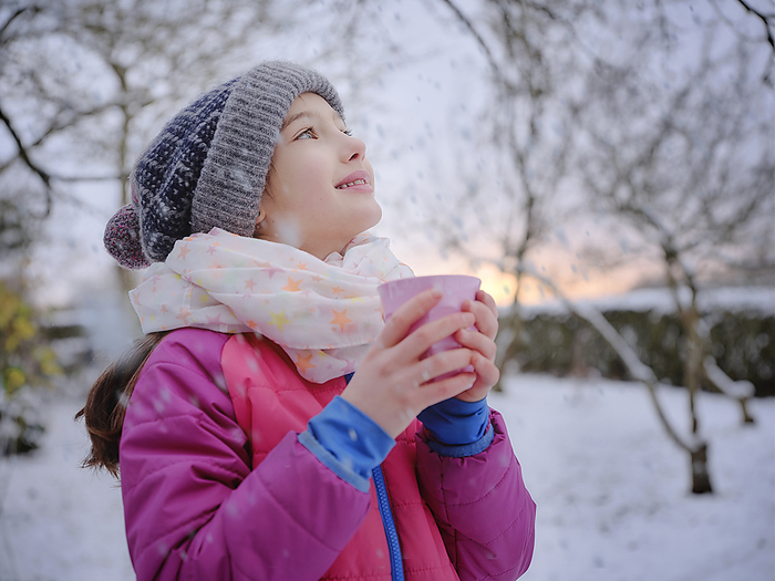 M dchen  9  schaut in den Himmel mit einer Tasse Tee im Schnee. Garten bei Sonnenuntergang. Malmsheim, BW, D. Smiling girl in warm clothing holding tea cup during winter