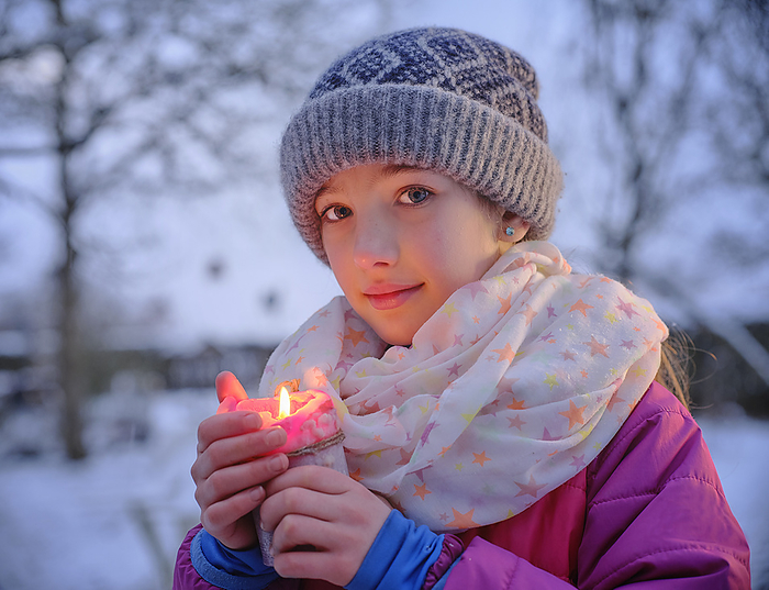 child Cute girl in warm clothing holding lit candle during winter