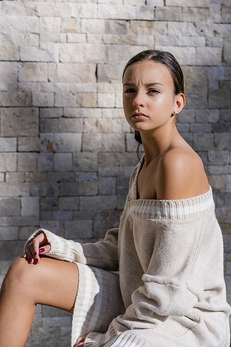 female Stylish teenage girl wearing off shoulder dress posing by brick wall at home