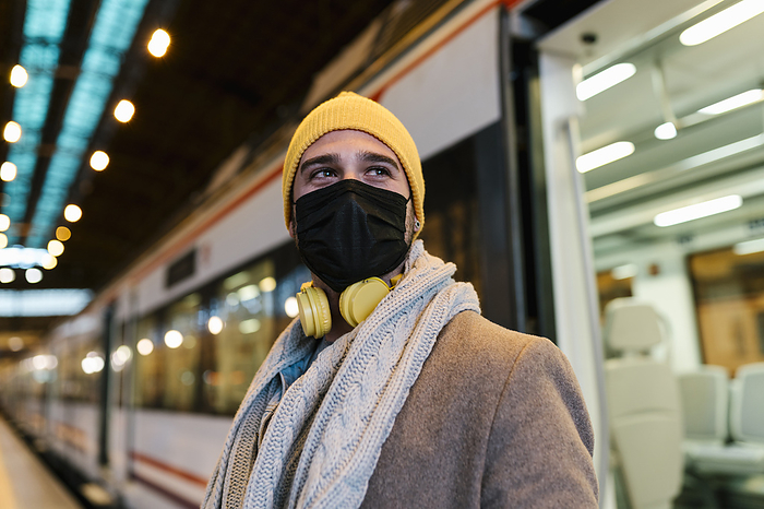Man wearing face mask looking away while standing against train at station