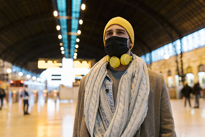 Man with face mask and headphones looking away while standing at station