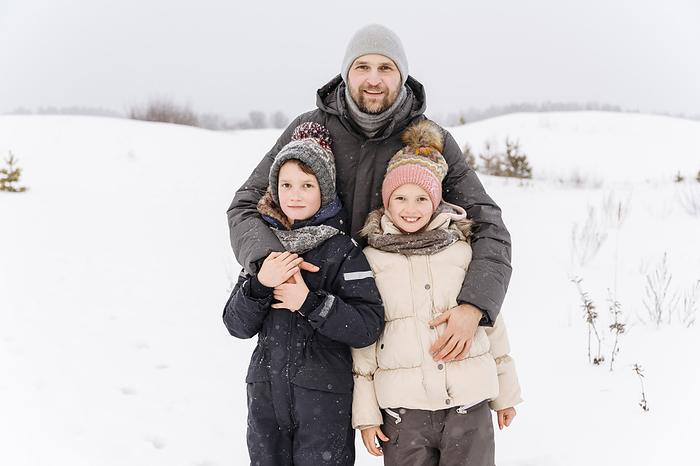 Russia, Moscow, portrait of father with two kids in winter landscape Smiling father with children standing on snow covered landscape against sky