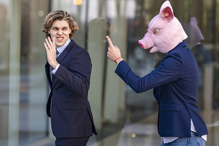 Young businessman in pig mask arguing with male colleague by glass wall