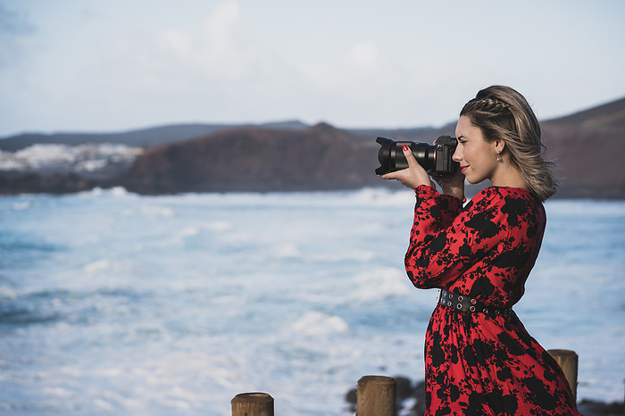  Young tourist girl visiting the viewpoint of  El golfo  in Lanzarote, Spain Young woman photographing with camera while standing against sea at El Golfo, Lanzarote, Spain