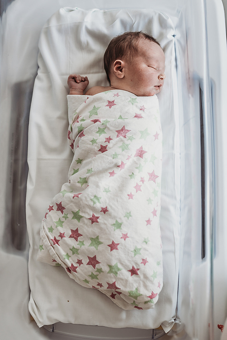 High angle of newborn baby boy in bassinet wrapped in hospital blanket