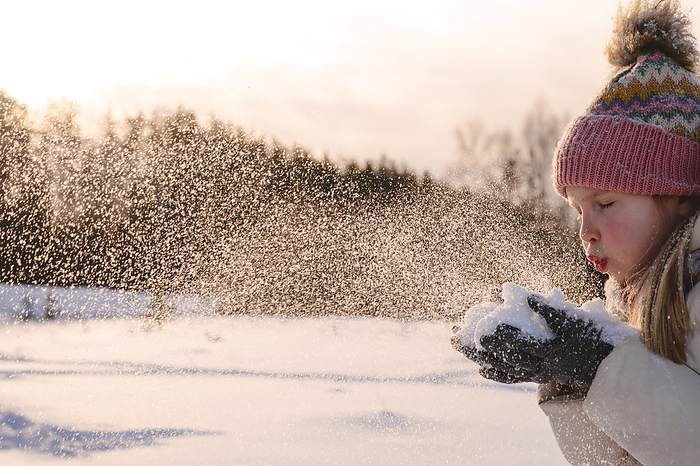 Moscow, Russia, girl playing with snow in winter landscape Playful girl in warm clothing blowing snow during winter