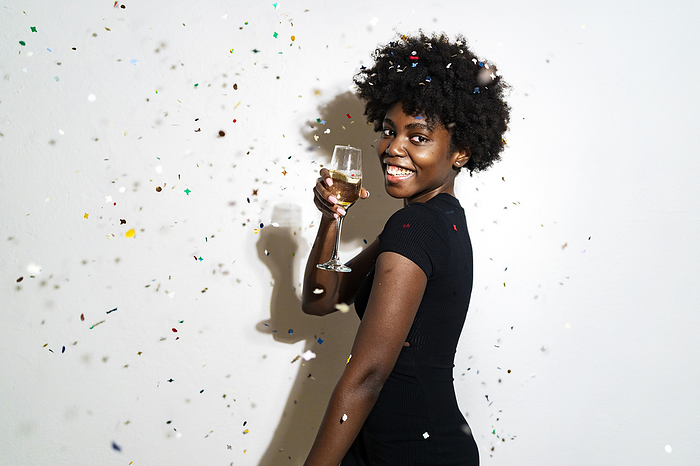 female Curly hair woman showing champagne flute while standing against white background