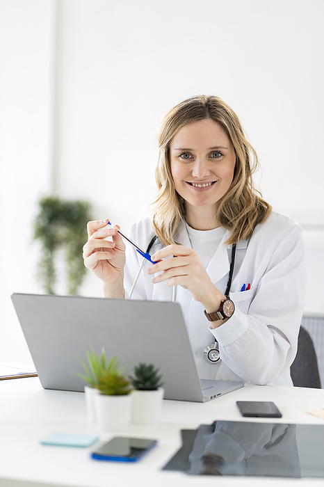 Adult woman doctor in a hospital, studio or clinic Smiling female doctor sitting with laptop at desk in medical clinic