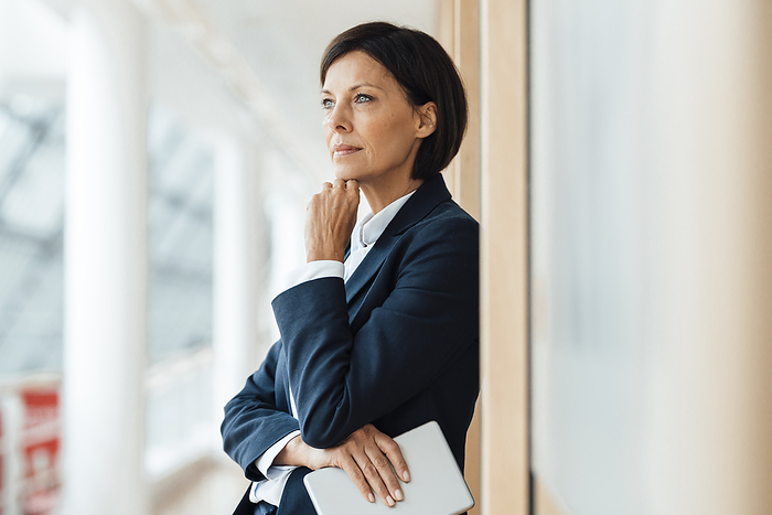 Thoughtful businesswoman with hand on chin against wall in office
