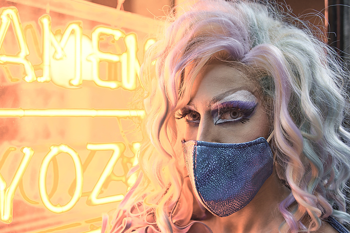 Confident drag queen in protective face mask by illuminated window