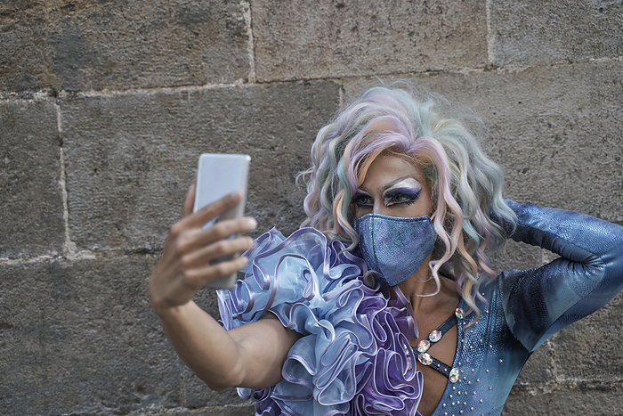 Drag queen taking selfie through smart phone against wall