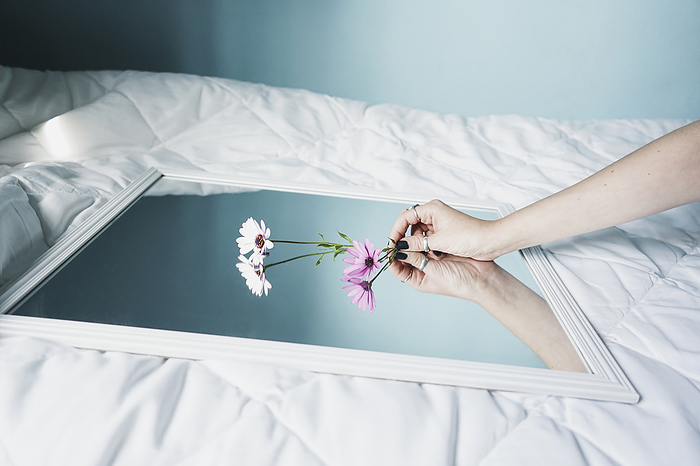 young woman Hand of young woman leaving daisies on mirror lying on white duvet