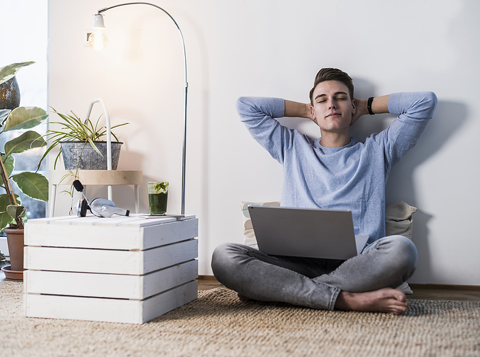 deutschland,mannheim,lifestyle,people,zuhause,office Young man with laptop relaxing while sitting against wall in living room