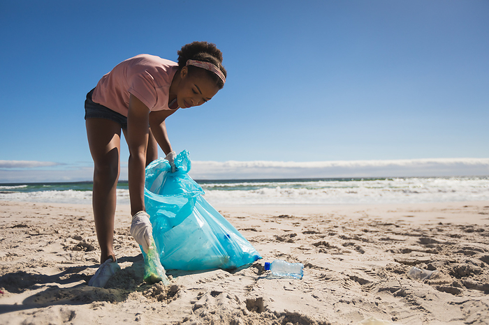African american woman wearing latex gloves collecting rubbish from the beach. eco summer beach conservation