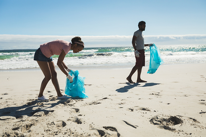 couple African american couple wearing latex gloves collecting rubbish from the beach. eco summer beach conservation