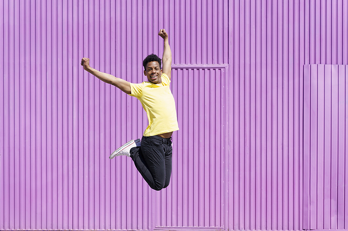 Carefree man jumping with arms raised by corrugated iron