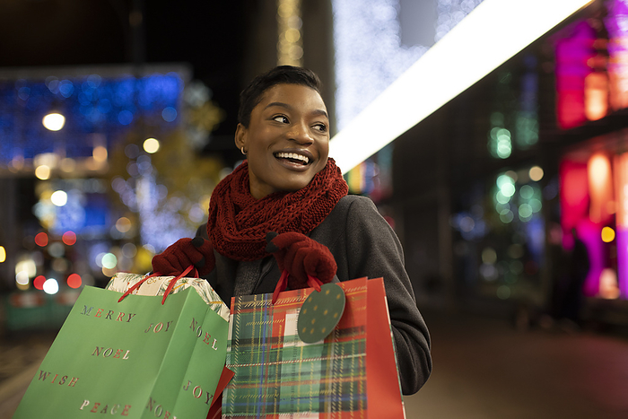 Happy young woman Christmas shopping in city at night