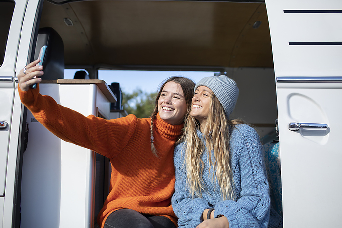 Happy young women friends taking selfie in camper van doorway