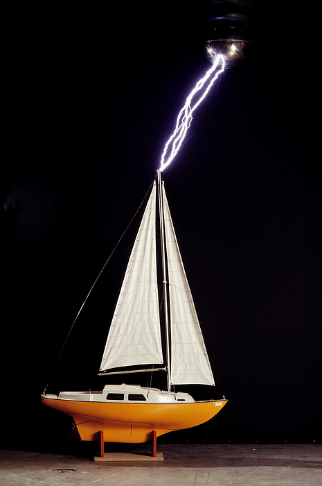 Lightning striking a sail boat model Simulated lightning strike to a sailboat model in a lab. Lightning occurs when a large electrical charge builds up in a cloud, probably due to the friction of water and ice particles. The charge induces an opposite charge on the ground, and a few leader electrons travel to the ground. When one makes contact, there is a huge backflow of energy up the path of the electron. This produces a bright flash of light, and temperatures of up to 30,000 degrees Celsius., Photo by PETER MENZEL SCIENCE PHOTO LIBRARY