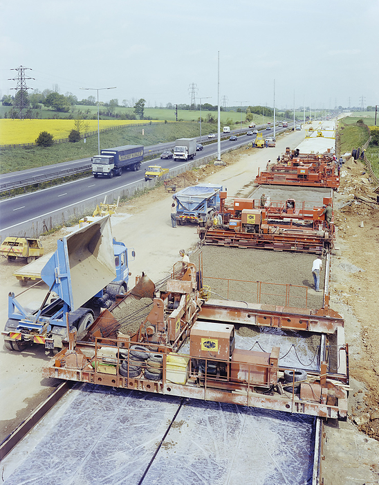 Slipform paving machines laying a road surface during widening works on the M1, 18 05 1982. Creator: John Laing plc. Slipform paving machines laying a road surface during widening works on the M1, showing concrete being tipped into the machine in the foreground. Starting in 1981, widening work was carried out on the M1 between Junctions 5  South Watford  and Junction 8  Hemel Hempstead . The aim was to convert the existing two lane carriageways from Junctions 5   7 and three lane carriageways from Junctions 7   8 into three lanes southbound, three lanes northbound from Junctions 5   6, and four lanes northbound from Junctions 6   8.