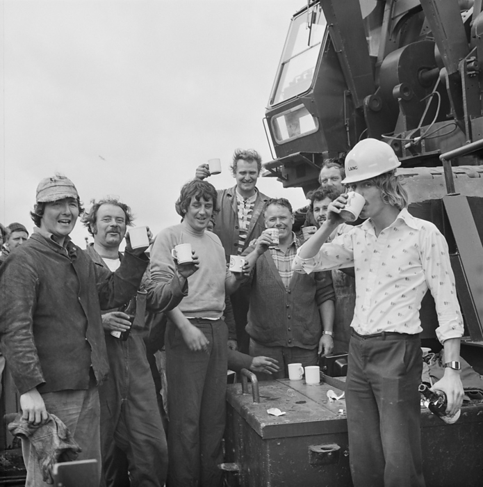 Peel Common Waste Water Treatment Works, Peel Common, Fareham, Hampshire, 21 06 1978. Creator: John Laing plc. A group of workers toasting the launch of a twin barge from Woolston, Hampshire, for use in the construction of the Peel Common Sewage Works outfall at Browndown. Laing Civil Engineering were contracted to construct the Browndown Outfall for the Southern Water Authority, as part of the South Hampshire Main Drainage Scheme for the treatment and disposal of sewage. Browndown Outfall is a 1km long underwater culvert which transports treated sewage from Peel Common Sewage Works, another contract carried out by Laing. The outfall was built in sections which were linked together in a chain on the seabed. The landward section of the outfall was cast in situ in a temporary cofferdam.