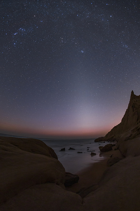 Zodiacal light over Persian Gulf coast, Iran Cone shaped zodiacal light glowing over the Persian Gulf, as seen from a rocky shore in southern Iran. Zodiacal light is the sunlight reflected by dust in the Solar System s plane. The Pleiades  Seven Sisters  star cluster, Mars and the bright star Aldebaran can be seen close to each other., Photo by AMIRREZA KAMKAR   SCIENCE PHOTO LIBRARY