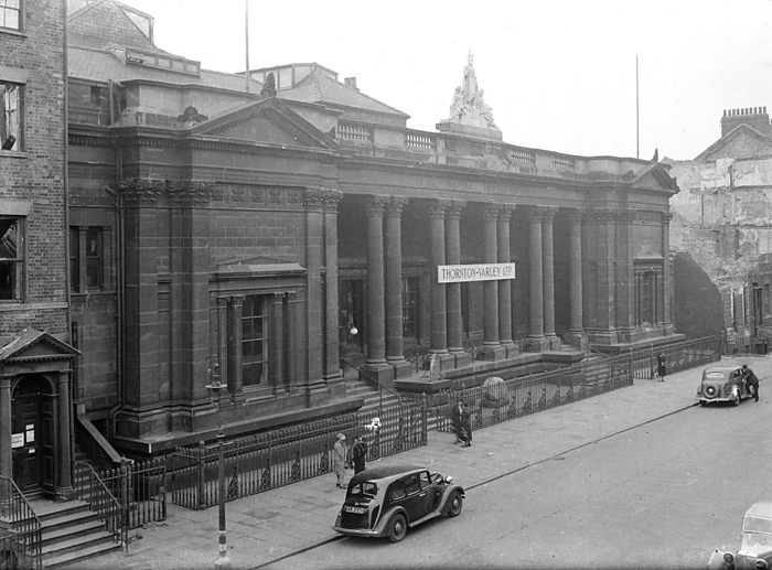 Royal Institute Museum, Albion Street, City of Kingston upon Hull, 1941. Creator: George Bernard Wood. Royal Institute Museum, Albion Street, City of Kingston upon Hull, 1941. An exterior view of the Royal Institute Museum, built in 1852 by Cuthbert Brodrick and destroyed by the Hull blitz. The museum was built by Cuthbert Brodrick  b.1821 d.1905  c 1852, with it opening in 1854. The Hull Literary and Philosophical Society was established in 1822 and resided at the museum. In c1941 the department store Thornton Varley Ltd relocated to the Royal Institue as it s former home had been damaged in the blitz. However, the institute was later bombed, c1943. The front facade had a large Corinthian portico of five bays, and two projecting bays on either side, with fluted columns surrounding the ground floor windows, and capped with a pediment. Above was a balustraded parapet and a central rectangular plinth with a statue, most likely of Britannia, with a spear in her right hand, and two figures reclining under her feet.