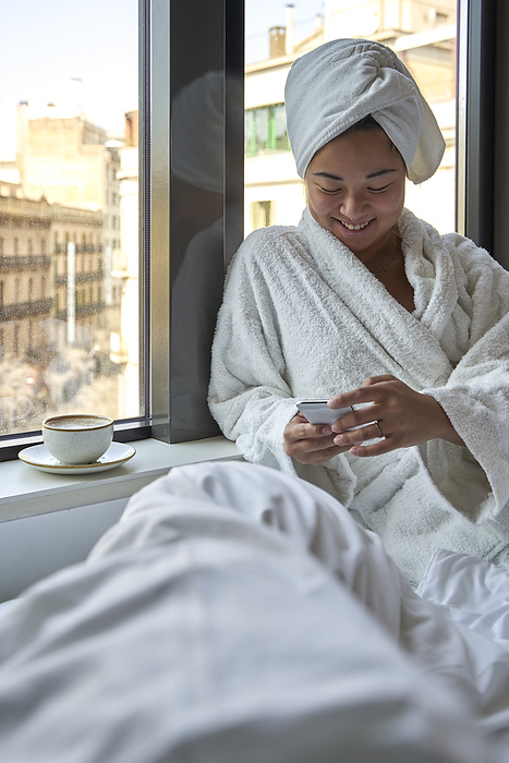 Smiling woman using smart phone while sitting on bed of hotel