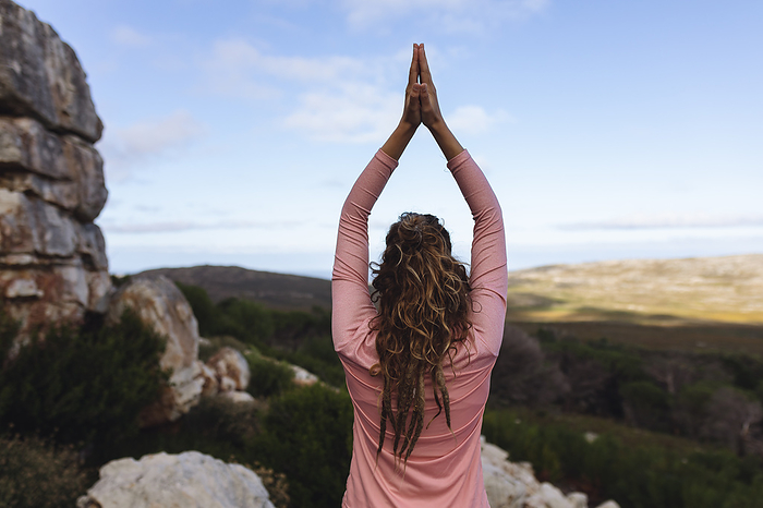 female Rear view of caucasian woman practicing yoga sitting with arms raised in rural mountain setting. healthy living, off grid and close to nature.
