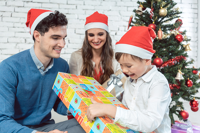 Child unwrapping Christmas present with his family Child unwrapping Christmas present with his family being excited