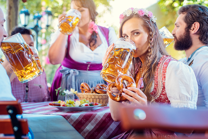 Woman in Tracht looking into camera while drinking a mass of beer Woman in Tracht looking into camera while drinking a mass of beer surrounded by her friends