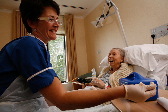 Nurse sitting on bed talking to patient Nurse in dark blue uniform sitting on the bed talking to a smiling elderly woman patient in a London hospital, prior to taking the patient s blood sample., Creditline:MEDICIMAGE   SCIENCE PHOTO LIBRARY
