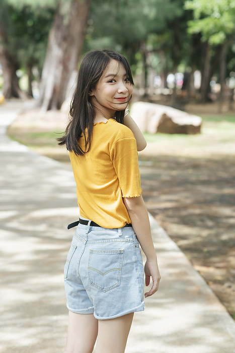 Black long hair girl in yellow t-shirt standing on the walk path in the park in summer.