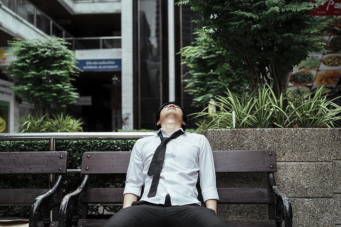 Exhausted asian business man taking nap on wooden bench. Business man sleeping on a bench after hardworking day.