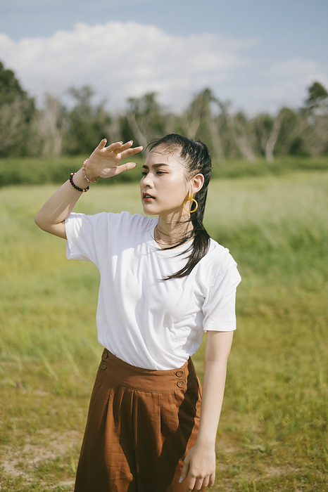 Black ponytail hair woman in casual clothes standing and walking in the grassland in sunny and windy day.