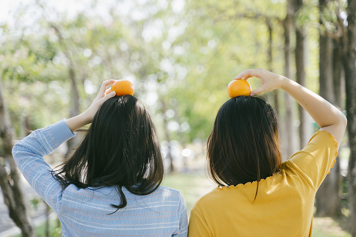 Two girls standing together and put the oranges on their head in the park.