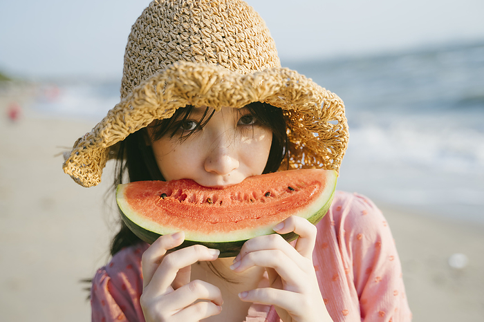 Woman eating watermelon Girl in brown hat bite the watermelon on the beach and smile.