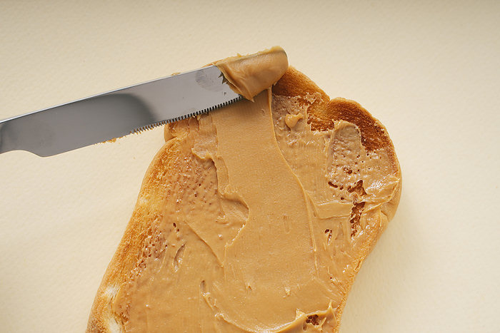Person using knife to put peanut butter on slice of bread.