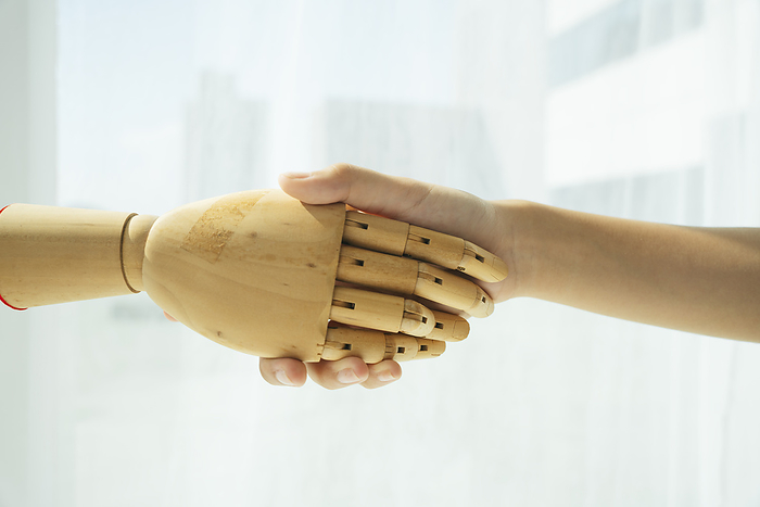 Hand of wooden cyborg robot and human shaking hand.