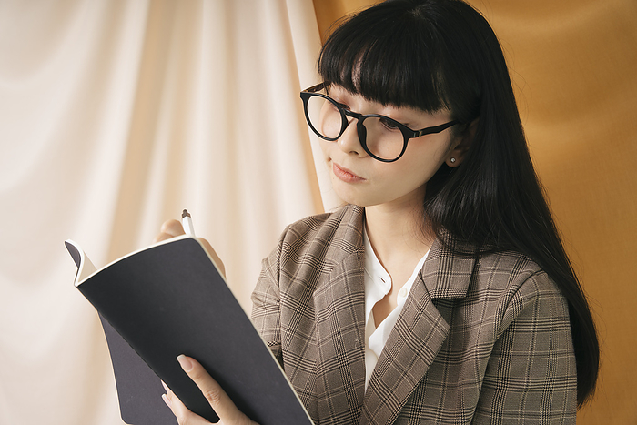 Beautiful businesswoman wearing eyeglasses and suit jacket looking a report on a book. Pretty nerd woman reading a book with thoughtful expression.