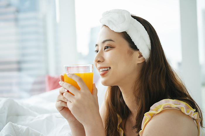 Young asian dark hair woman wearing white headband holding glass of orange juice.