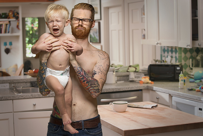 Caucasian man holding crying baby son in kitchen