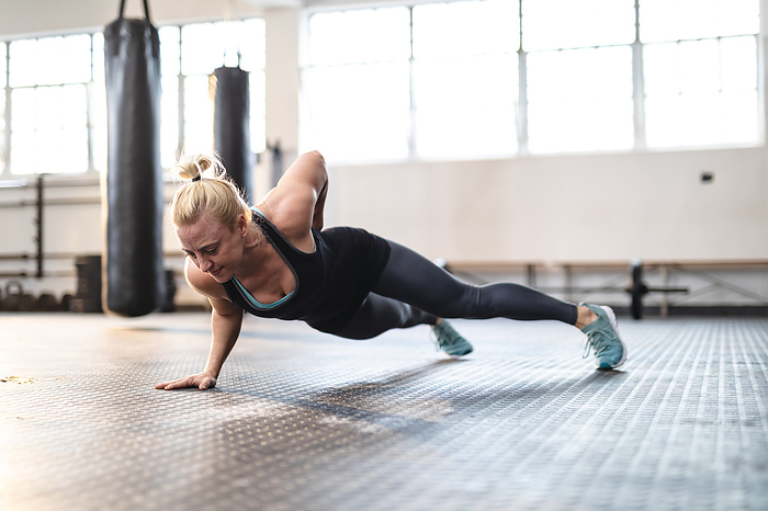 Strong caucasian woman exercising at gym, doing push-ups using one hand. strength and fitness cross training for boxing.