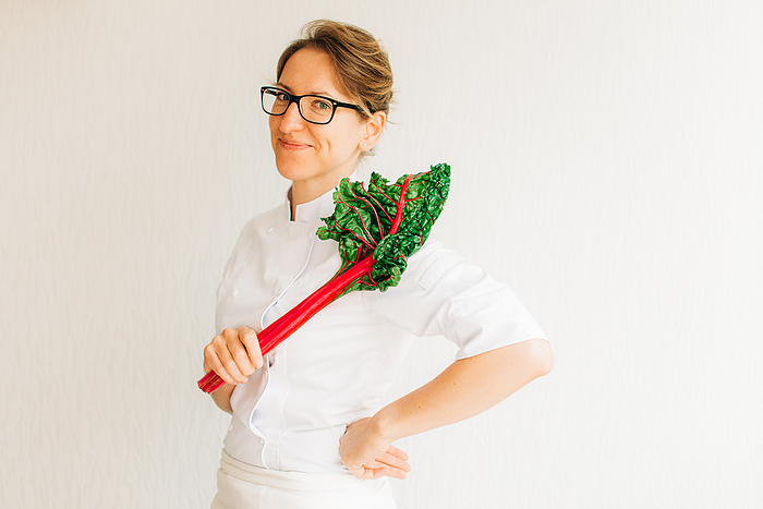 Woman chef in uniform holding swiss chard leaf on white background