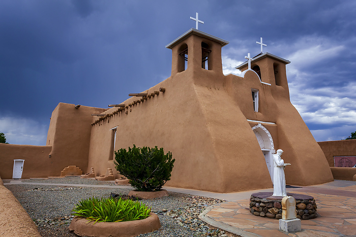 America Side view of the historic San Francisco de Asis Church with a statue of San Francisco of Asis in the landscaped courtyard, located on the main plaza of Ranchos de Taos  Taos, New Mexico, United States of America  , Photo by Lyle Johnson   Design Pics